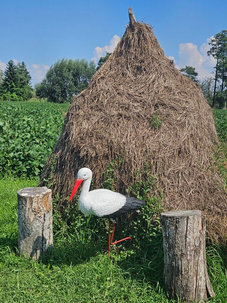A stork decoration on the grass next to a large pile of hay.